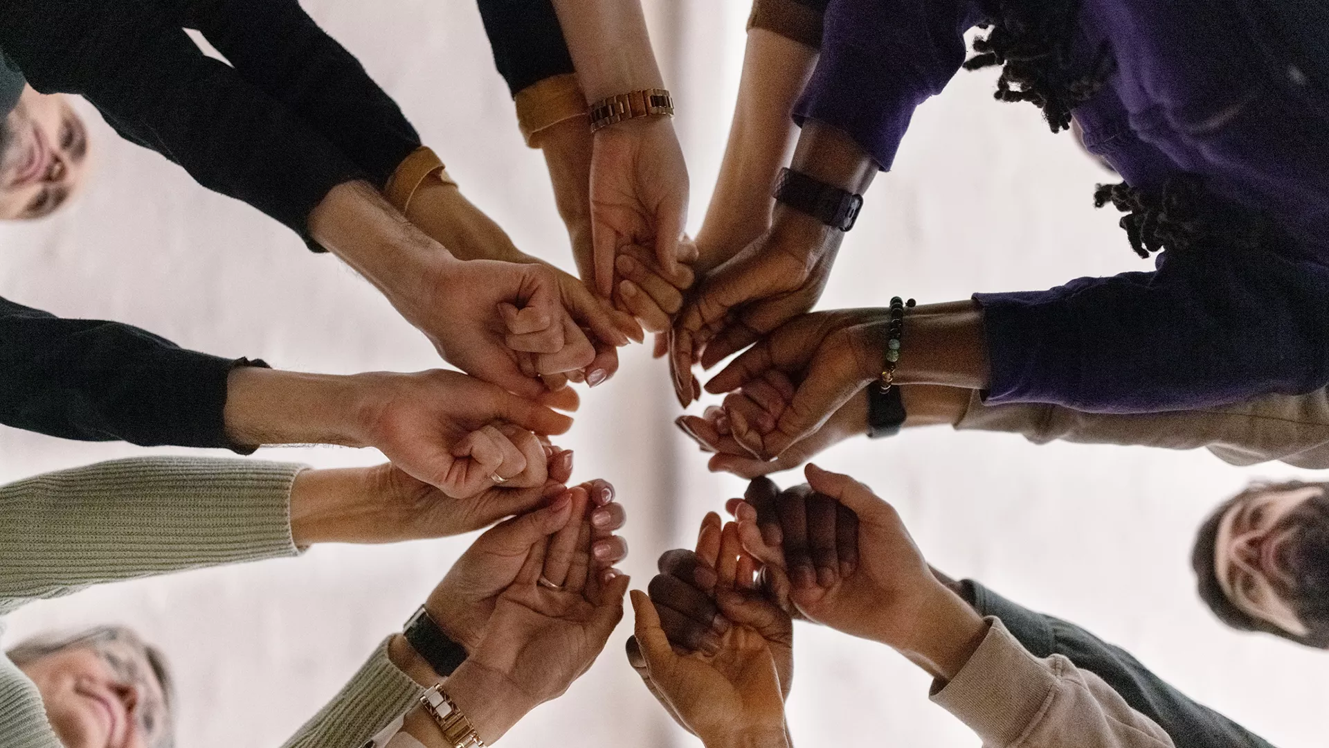 An image of five people putting their knuckles together to great a circle.